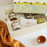 Gift box with candles and a 'Happy Diwali' card on a white surface with an orange fabric.