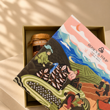 A gift box containing a jar of nuts and honey and a colorful illustrated card or booklet from Roses & Tulip, placed on a beige surface with soft shadows.