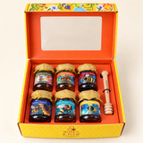 Open orange gift box containing six Roses & Tulip honey varieties and a wooden honey dipper.