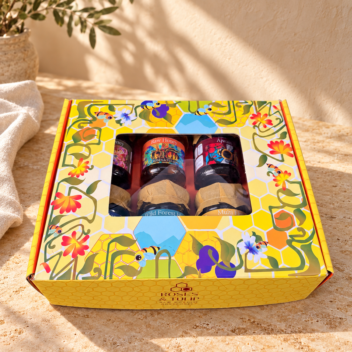 Roses & Tulip honey gift box on sunlit stone, with jars partially visible through the printed lid’s window